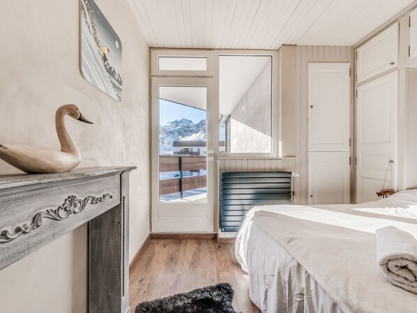 Une chambre avec une commode en bois, une décoration en forme de cygne, un lit avec une serviette roulée et une vue sur les montagnes par la porte.