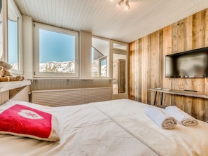 Quarto com cama, TV e janela com vista para as montanhas.