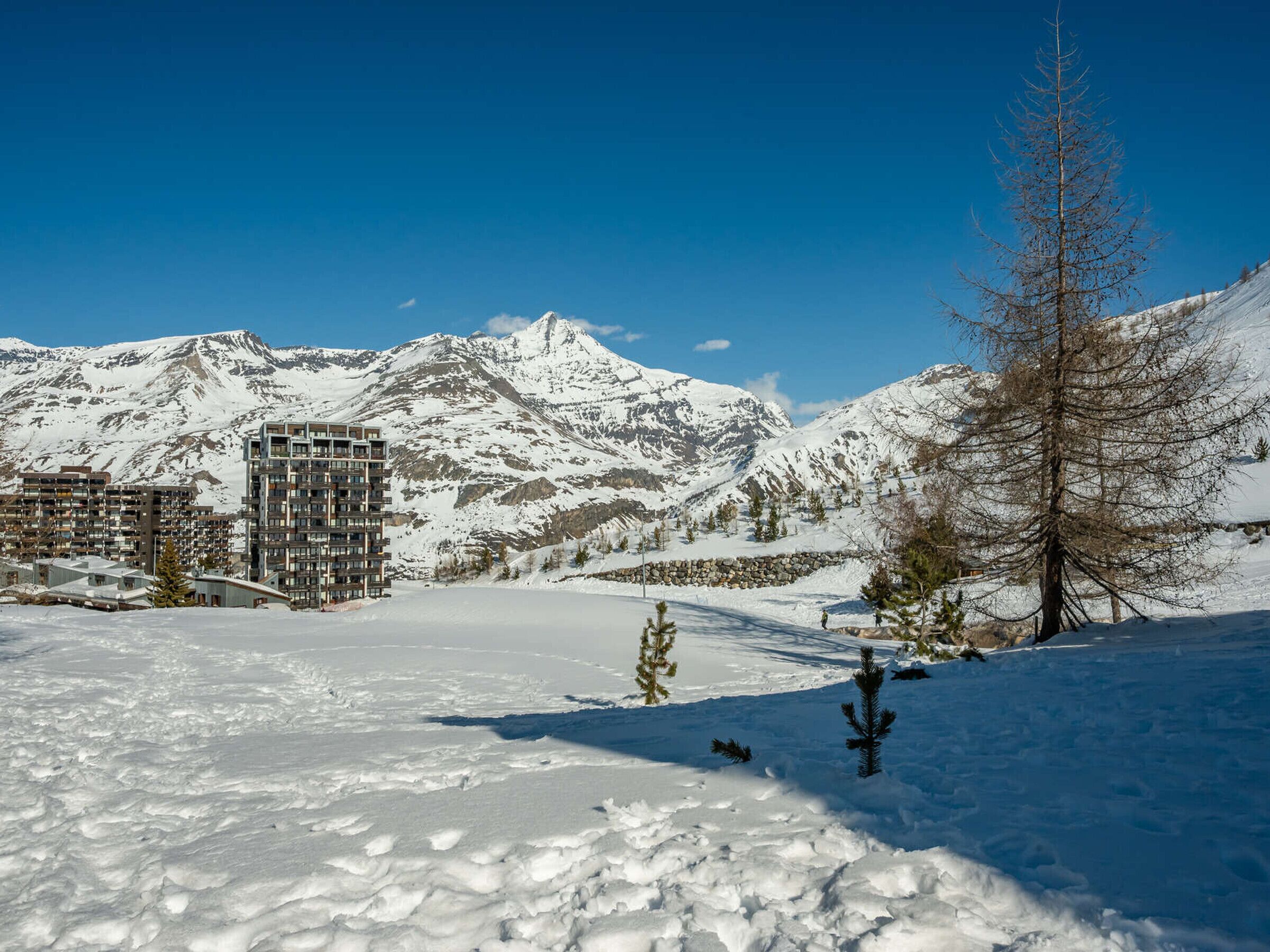 Un paysage enneigé, avec une chaîne de montagnes en arrière-plan et un bâtiment à plusieurs étages au premier plan.