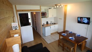 Un espace de vie compact comprenant un coin cuisine, un coin repas et un téléviseur fixé au mur.