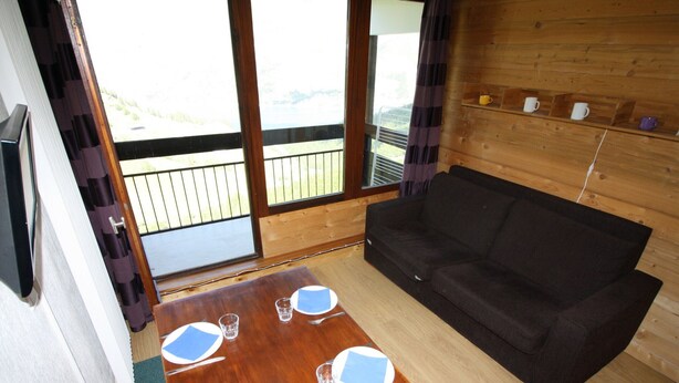 Une cabane en bois avec une table à manger dressée pour quatre personnes, un canapé noir et un balcon doté de balustrades en bois.
