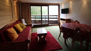 A cozy room with a wooden sofa, a dining table, and a large window offering a view of a lake. - Large Studio for 4 - Lake View in Tignes (Tignes)