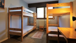 Une chambre de dortoir avec des lits superposés, un petit bureau, une chaise, un radiateur et une fenêtre.