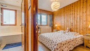 A bedroom with a wooden wall, a bed with floral bedding, a nightstand, a lamp, and a teddy bear. - Apartment 3*, Savoyard style, 4 ppl, renovated, lake (Tignes)