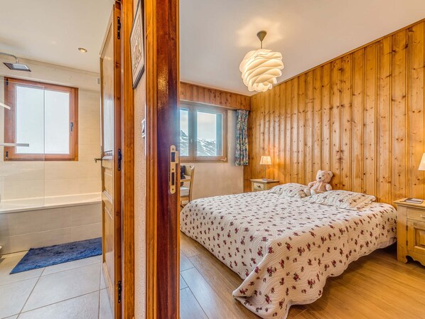 Un dormitorio con pared de madera, una cama con ropa de cama floral, una mesita de noche, una lámpara y un oso de peluche.