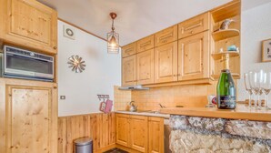 A kitchen with wooden cabinets, a stone countertop, a microwave, a sink, and a trash bin. - Apartment 3*, Savoyard style, 4 ppl, renovated, lake (Tignes)
