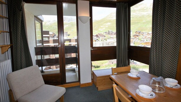 Una stanza accogliente con un tavolo di legno apparecchiato per la colazione, una sedia e vista su un villaggio montano attraverso ampie finestre.