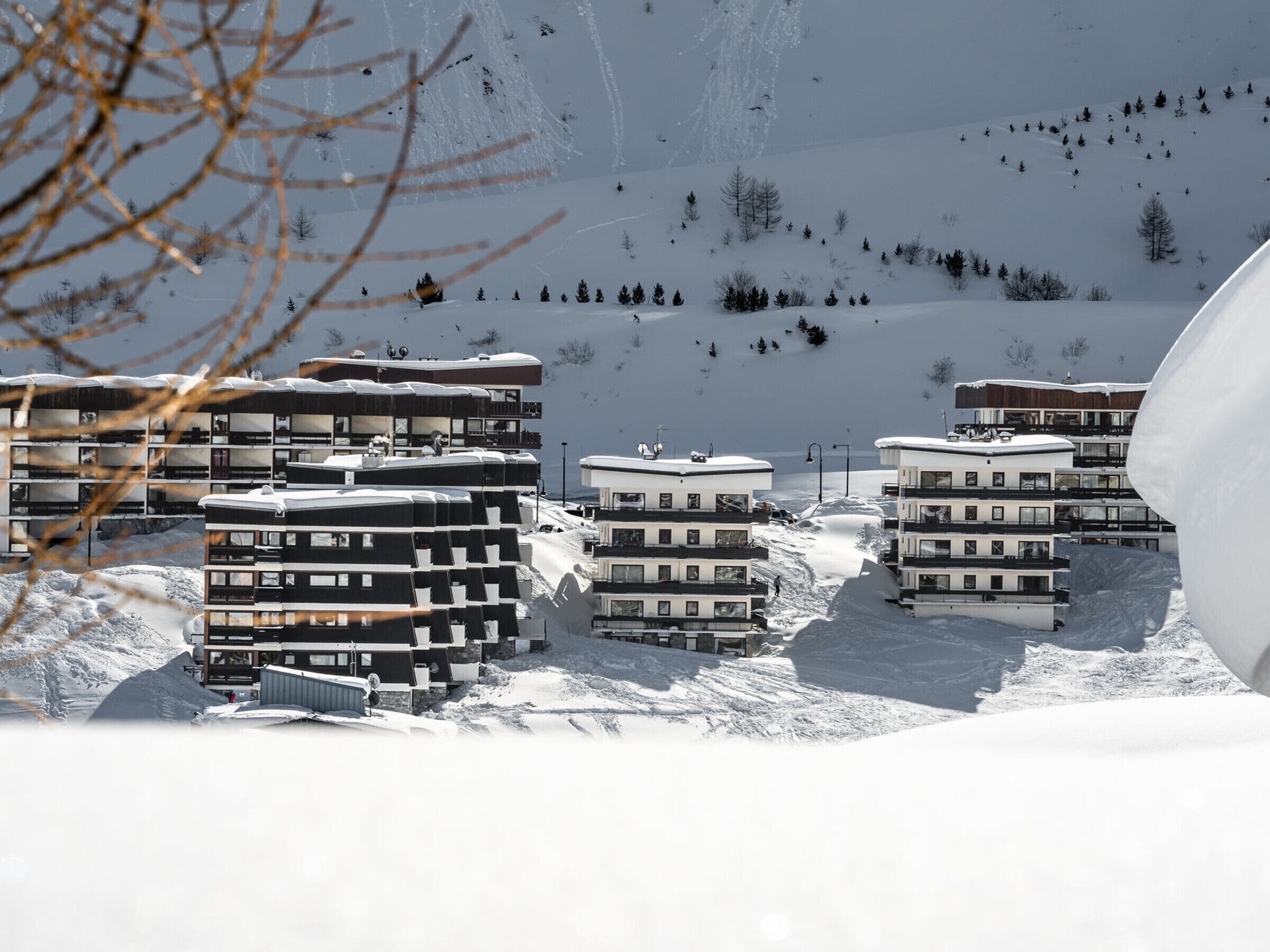 Een besneewd berglandschap met moderne, meer verdiepingen tellende gebouwen, waarschijnlijk een skigebied.