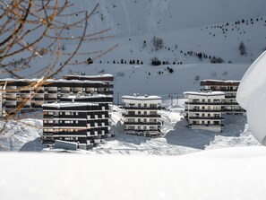 Zona montañosa nevada con edificios modernos de varios pisos, probablemente un centro de esquí.