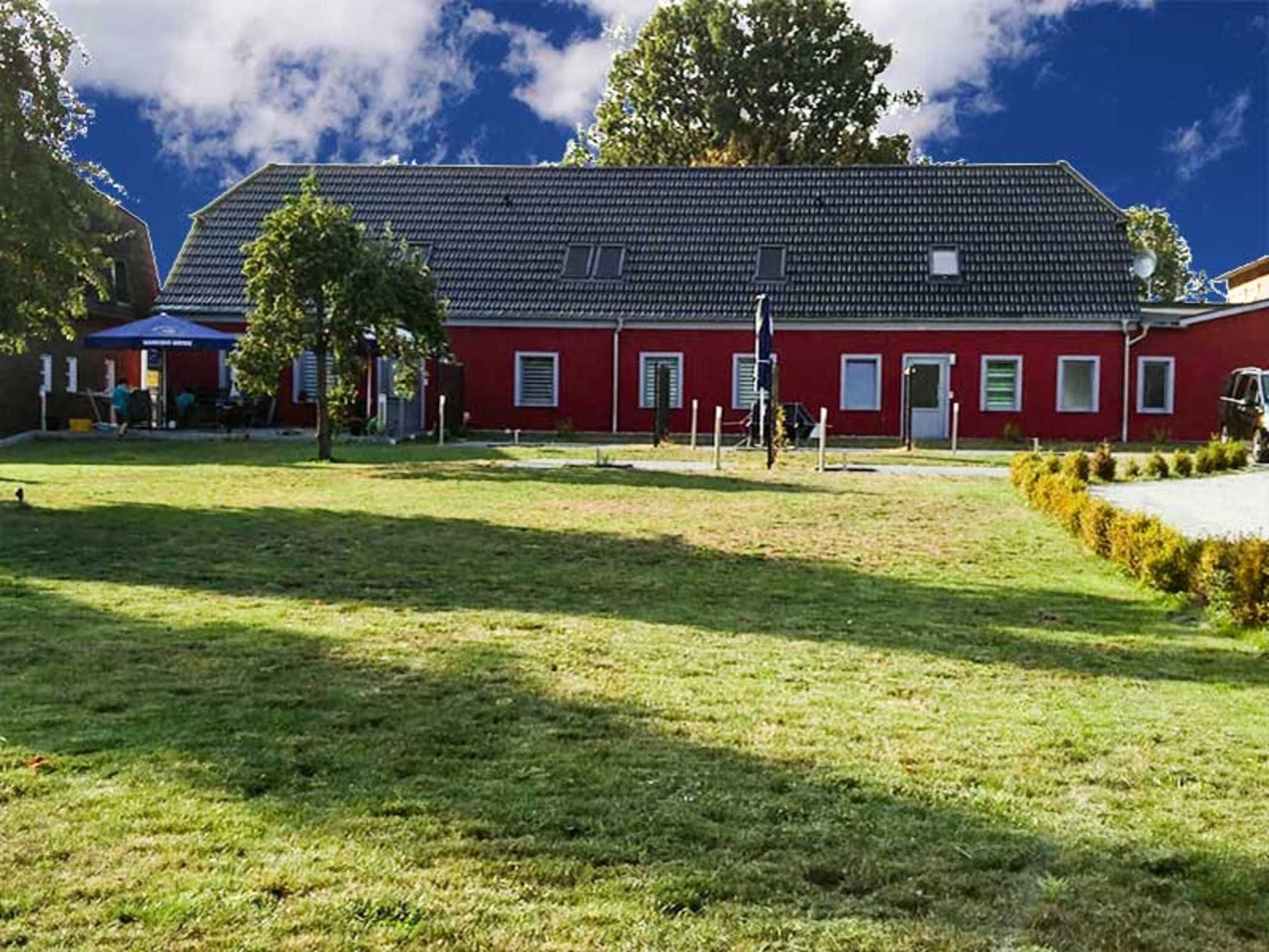Ein rotes Gebäude mit geneigtem Dach, umgeben von einer Rasenfläche und Bäumen.