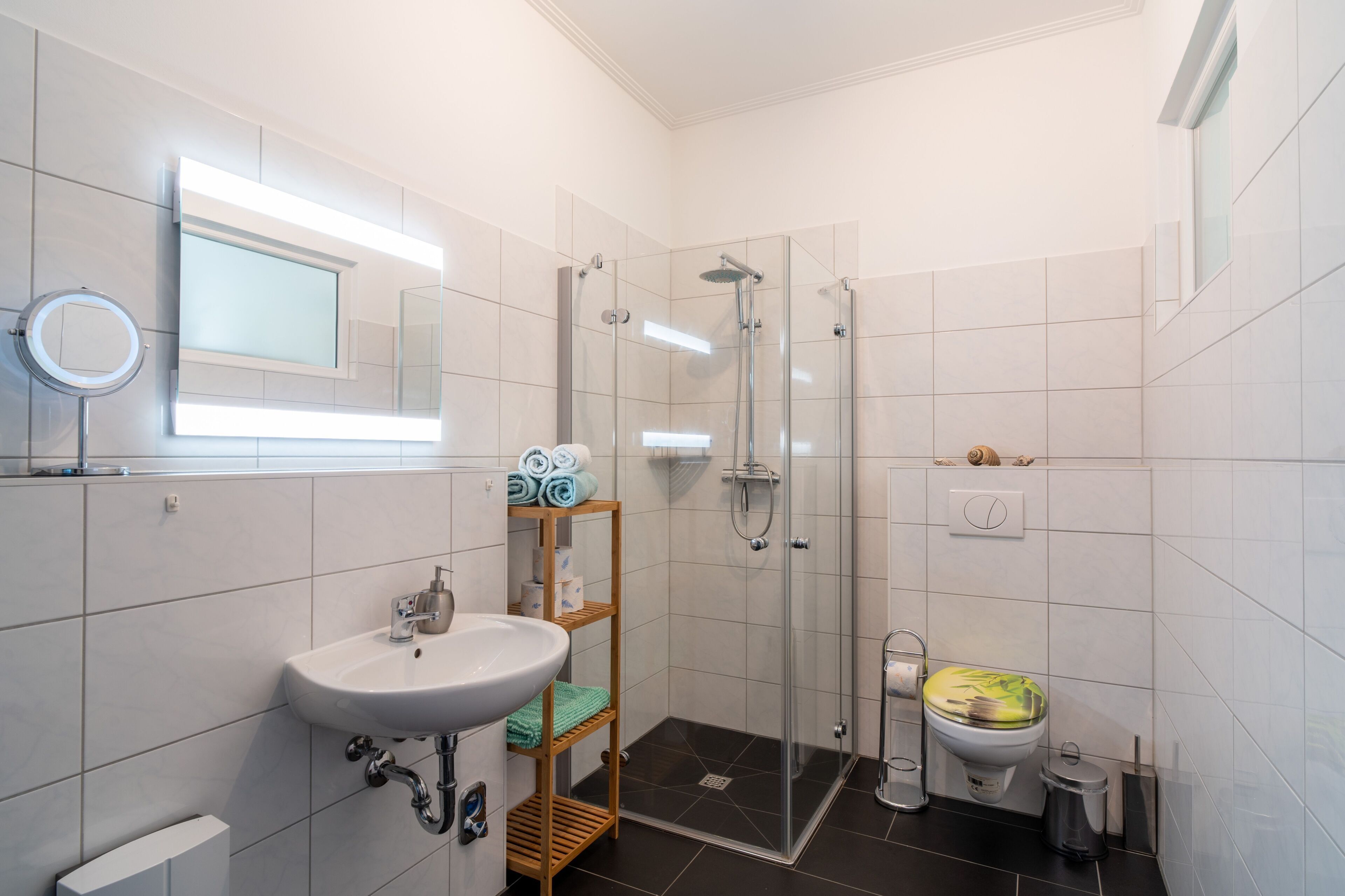 Een badkamer met een wastafel, spiegel, douche, toilet en een plank met handdoeken.