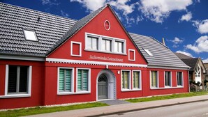 A red building with a gabled roof, a central entrance with a door, and a sign above the entrance.