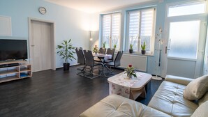 A living room with a TV, sofa, dining table, chairs, and potted plants.
