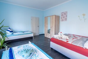 Une chambre avec deux lits, une armoire, un miroir et un mur orné d’un tableau représentant des motifs floraux.