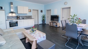 A modern living room with a sofa, a coffee table with flowers, a TV, and a dining area with chairs and a table.