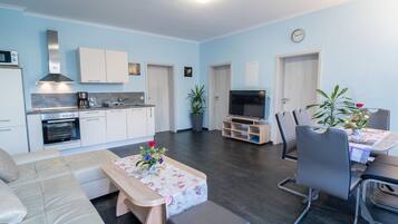 Ein modernes Wohnzimmer mit einer Couch, einem Couchtisch mit Blumen, einem Fernseher und einem Essbereich mit Stühlen und einem Tisch.