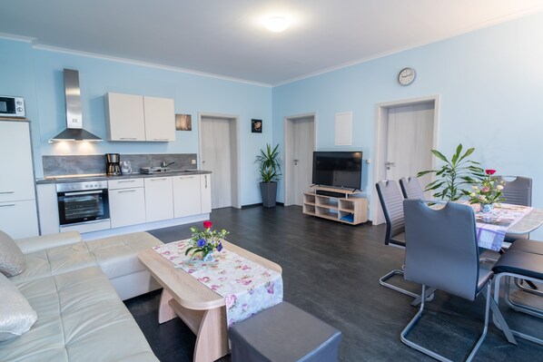 Un salon moderne avec un canapé, une table basse décorée de fleurs, un téléviseur et un coin repas comprenant des chaises et une table.