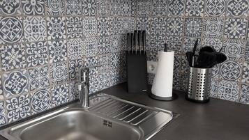 A kitchen with a stainless steel sink, white cabinets, and patterned tile backsplash.