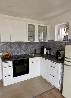 A modern kitchen with white cabinets, a built-in oven, a coffee maker, and a fruit bowl on the counter.