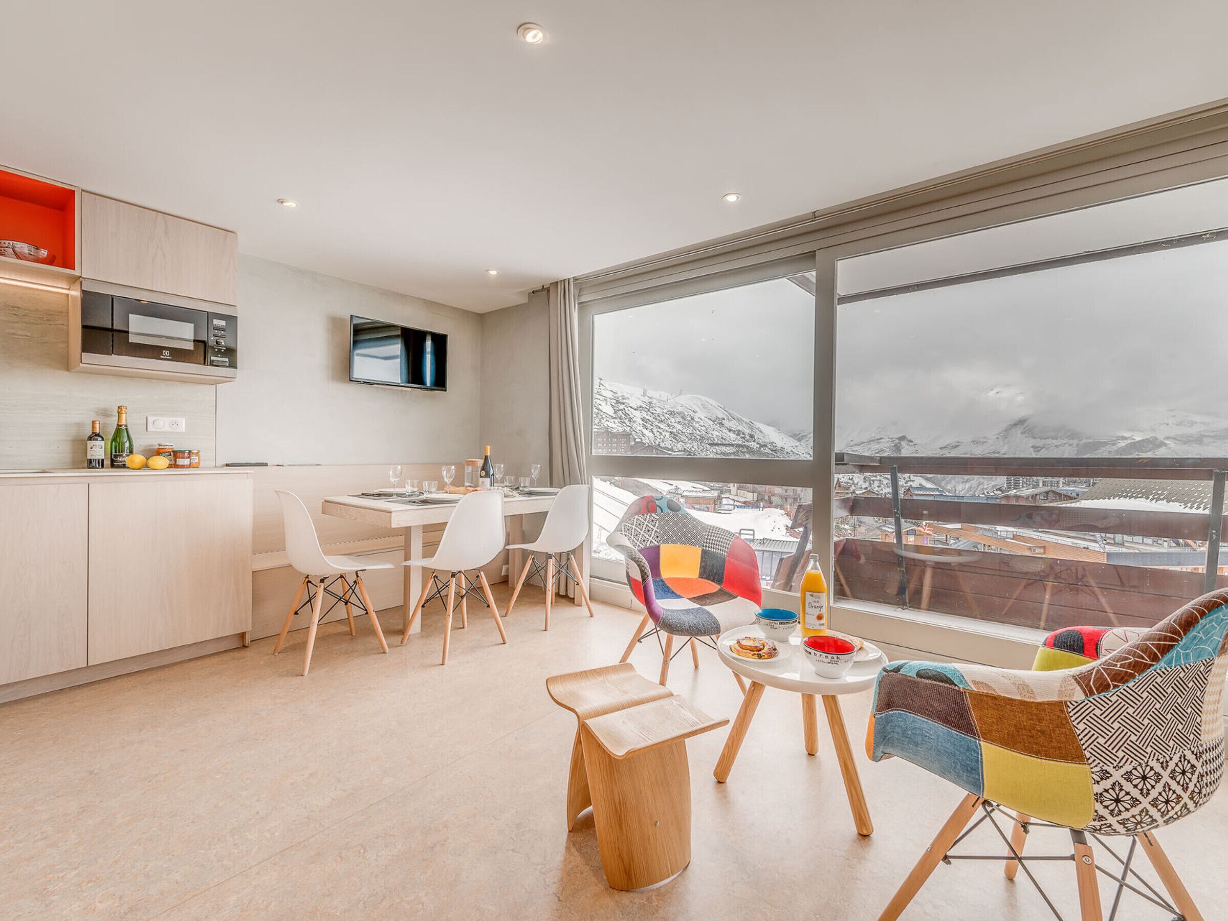A modern kitchen with a dining area, large windows with a snowy view, and colorful chairs.