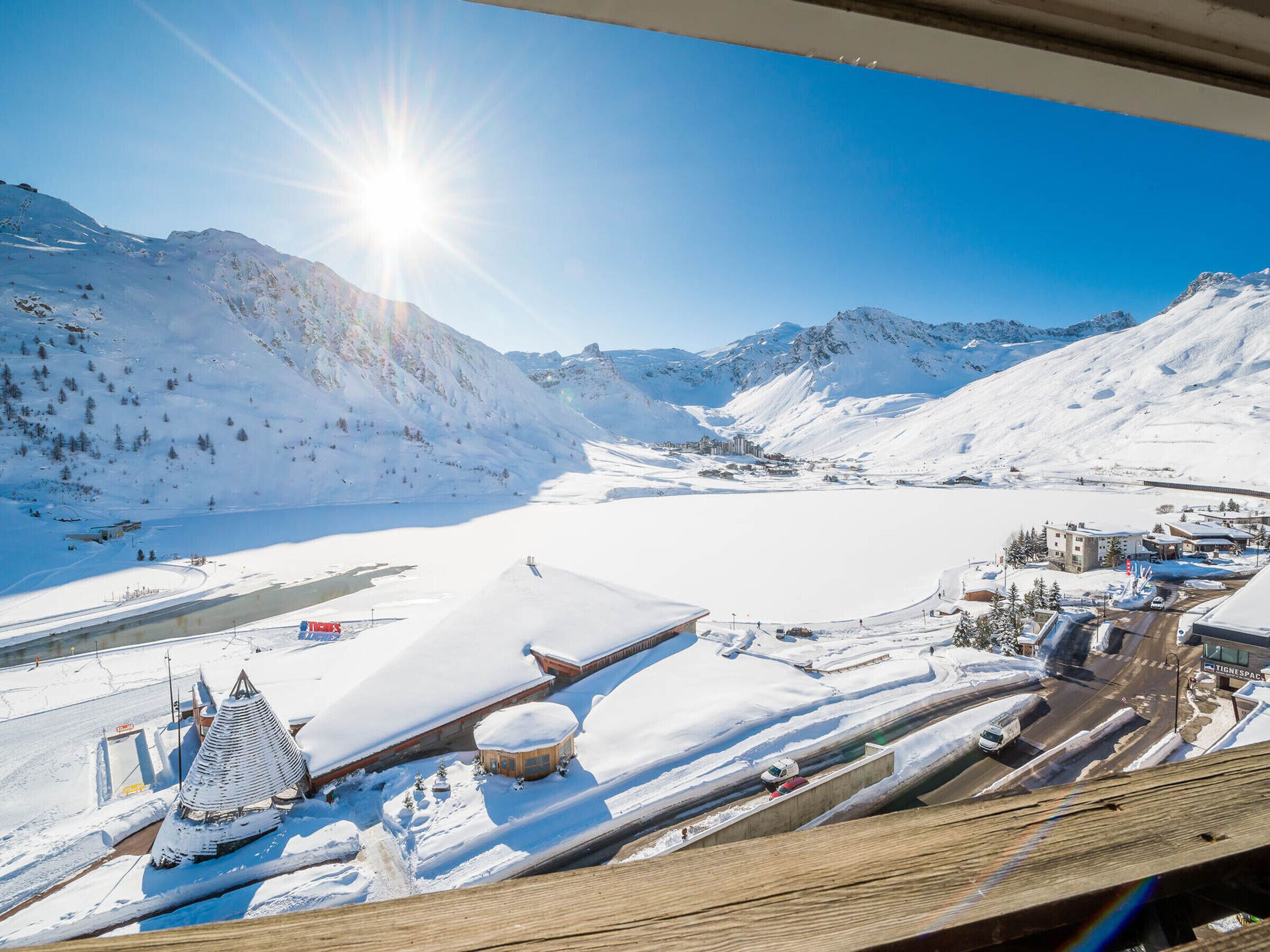 A snow-covered mountain landscape with a ski resort, including a ski lift, buildings, and a clear sky.