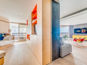 A modern living room with a sofa, a coffee table, and a TV. There is a sliding door leading to a balcony with a view of a snowy landscape.