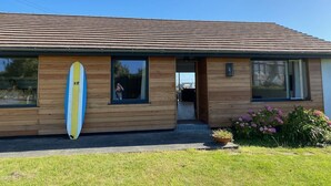 A modern house with a wooden exterior, a large window, and a surfboard leaning against the wall.