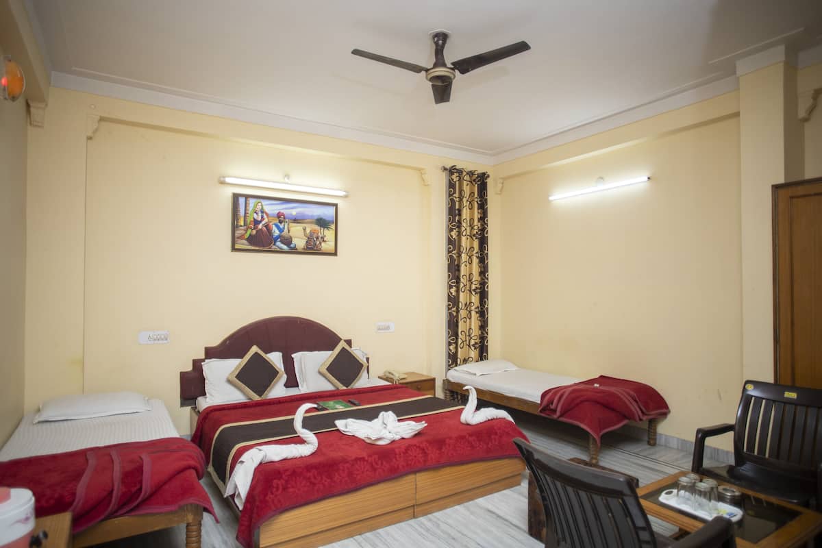 A hotel room with two single beds, a wooden headboard, a ceiling fan, a small table with a chair, and a wall-mounted painting.