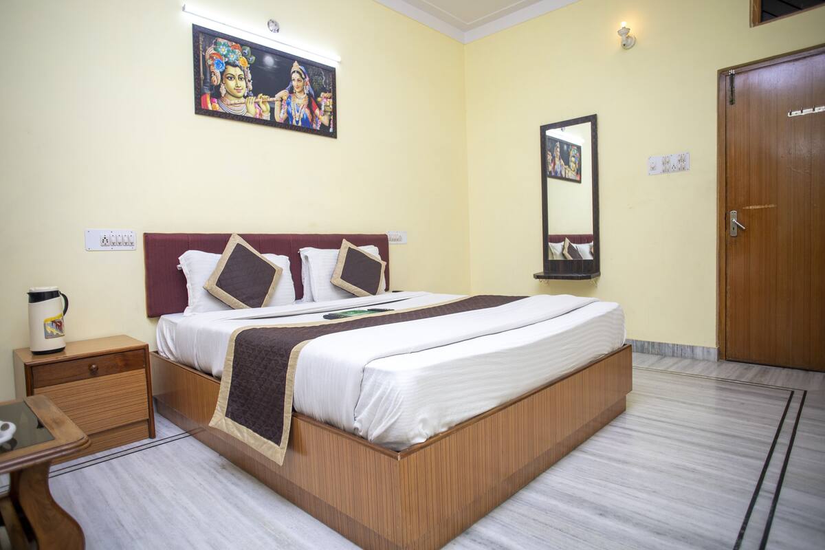 A hotel room with a large bed, a nightstand, a bedside table, a wall-mounted TV, a mirror, and a door.