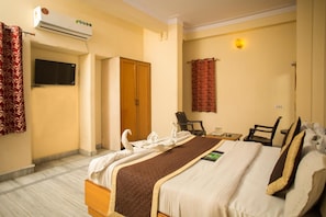 A hotel room with a bed, a desk, a chair, an air conditioning unit, and a television.