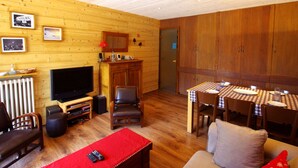 Un salon chaleureux avec un décor intérieur en bois, une télévision, une table à manger dressée pour quatre personnes et un canapé.