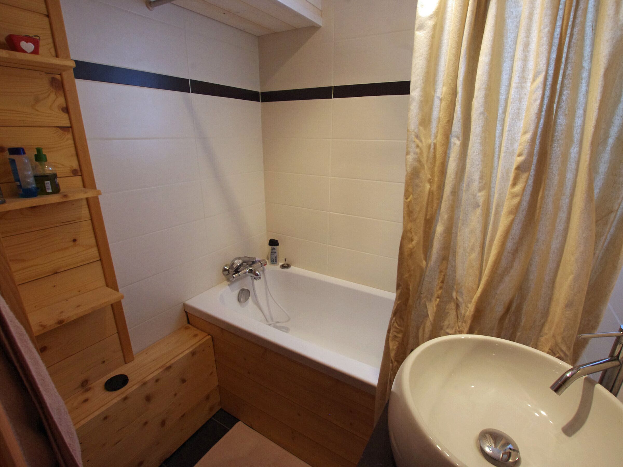 Une petite salle de bain avec une étagère en bois, une baignoire et un lavabo.