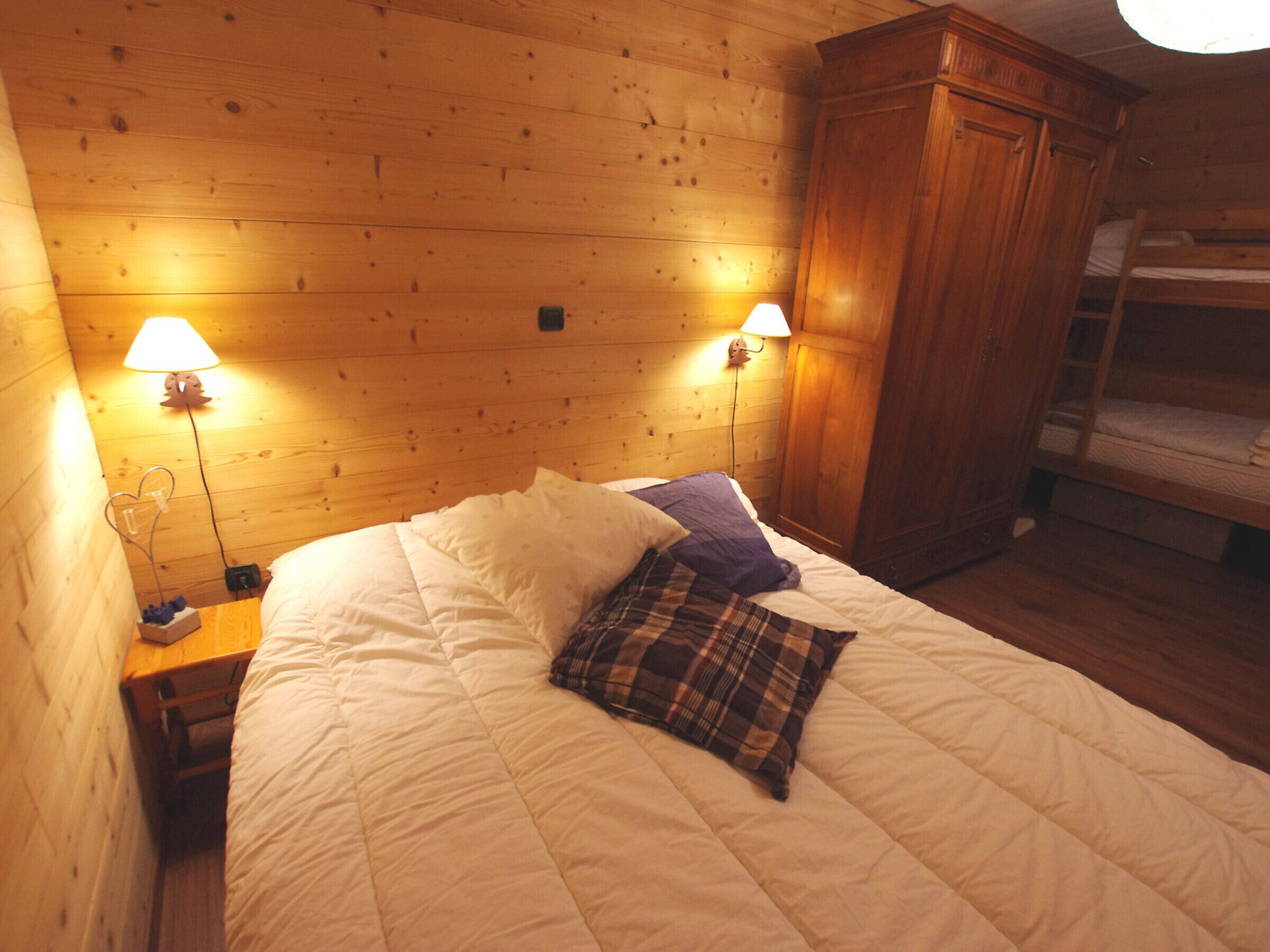 Une pièce aménagée comme un chalet en bois, avec un lit, deux lampes fixées au mur et une armoire en bois.