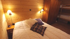 Une pièce aménagée comme un chalet en bois, avec un lit, deux lampes fixées au mur et une armoire en bois.