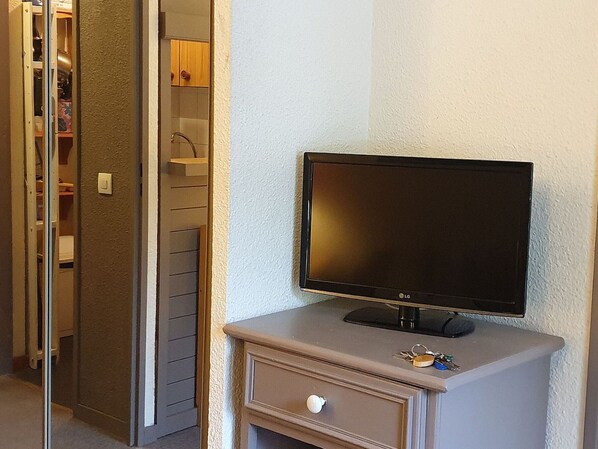 A television on a small cabinet in a room with a door leading to a closet.