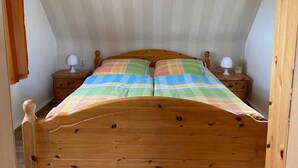 A bedroom with a sloped ceiling, a wooden bed with a plaid bedspread, two bedside tables with lamps, and a wooden wardrobe.