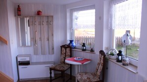 A small kitchen with wooden cabinets, a white countertop, two chairs, a small table with a red tablecloth, and a window with a view of a fence.