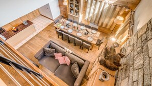 A spacious loft-style living area with a dining table set for four, a cozy seating area with a sofa, and a stone wall. - 5* Chalet in Tignes: 6 rooms, sauna, jacuzzi, parking (Tignes-Les Brévières)
