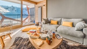 Ein modernes Wohnzimmer mit grauem Sofa, Holztisch und Blick auf einen verschneiten Berg.