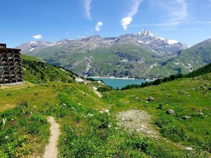A mountain landscape with a lake, a path, and a building with balconies.