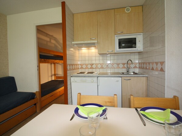 A compact kitchen with a microwave, sink, and dishwasher. There's a small dining table with chairs and a bunk bed in the corner.