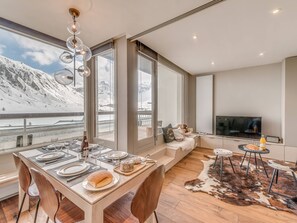 A modern kitchen with a large island, dining area, and a cozy seating area with a view of a snowy mountain landscape. - Renovated 3* apartment with terrace, lake view, sleeps 6, WiFi included (Tignes)