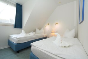 Een hotelkamer met twee bedden, een raam met blauwe gordijnen en uitzicht op de stad.