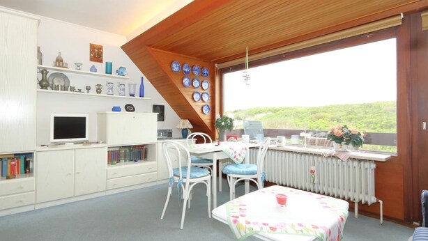 A cozy room with a dining table, chairs, a TV, and a bookshelf. - App. Feusser - at Wenningstedter Strand (Wenningstedt-Braderup (Sylt))