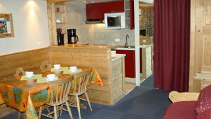 A compact kitchen with a microwave, coffee maker, and red cabinets. There is a dining area with a table set for four and a red curtain. - Large studio for 4 - Comfortable with balcony (Tignes)