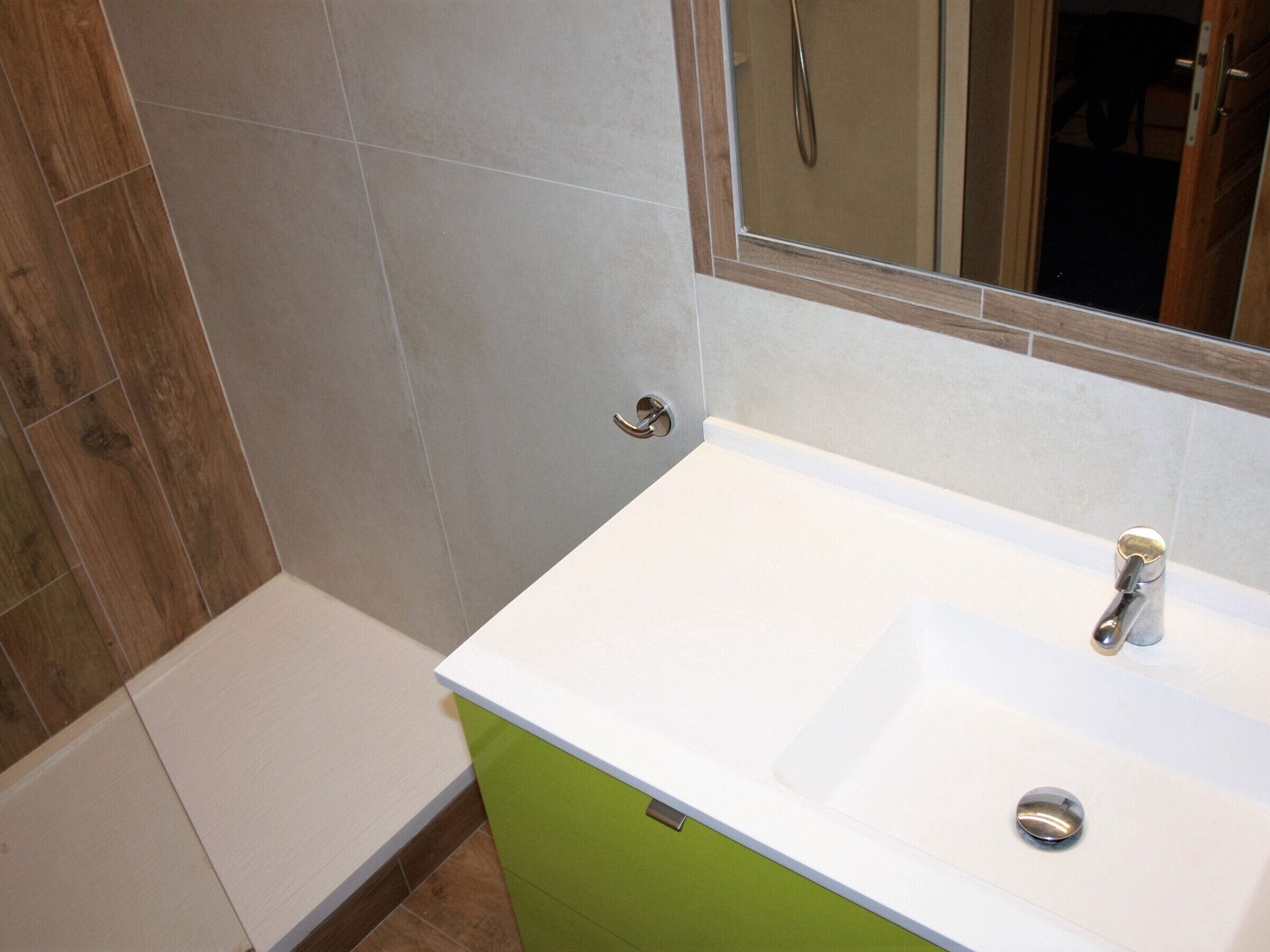Een badkamer met een witte wastafel, een groen kastje en een spiegel erboven.