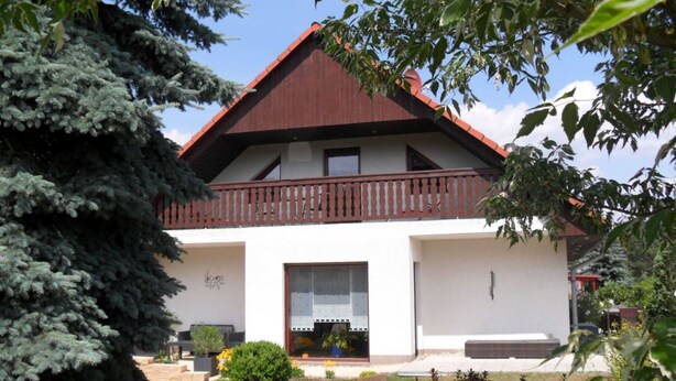 Una casa de dos pisos con un balcón, un ventanal grande y un pequeño porche.