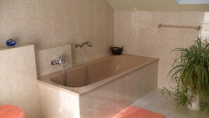 Un baño con bañera, inodoro y lavabo. Hay un perchero y una planta en maceta.
