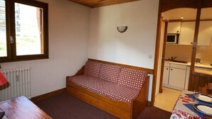 Una camera accogliente con soffitto in legno, un divano con rivestimento decorativo, un tavolo da pranzo per due persone e un angolo cottura con forno a microonde e lavello.