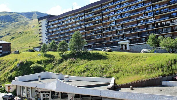 Un hotel a più piani con balconi, sullo sfondo di colline e montagne verdi.